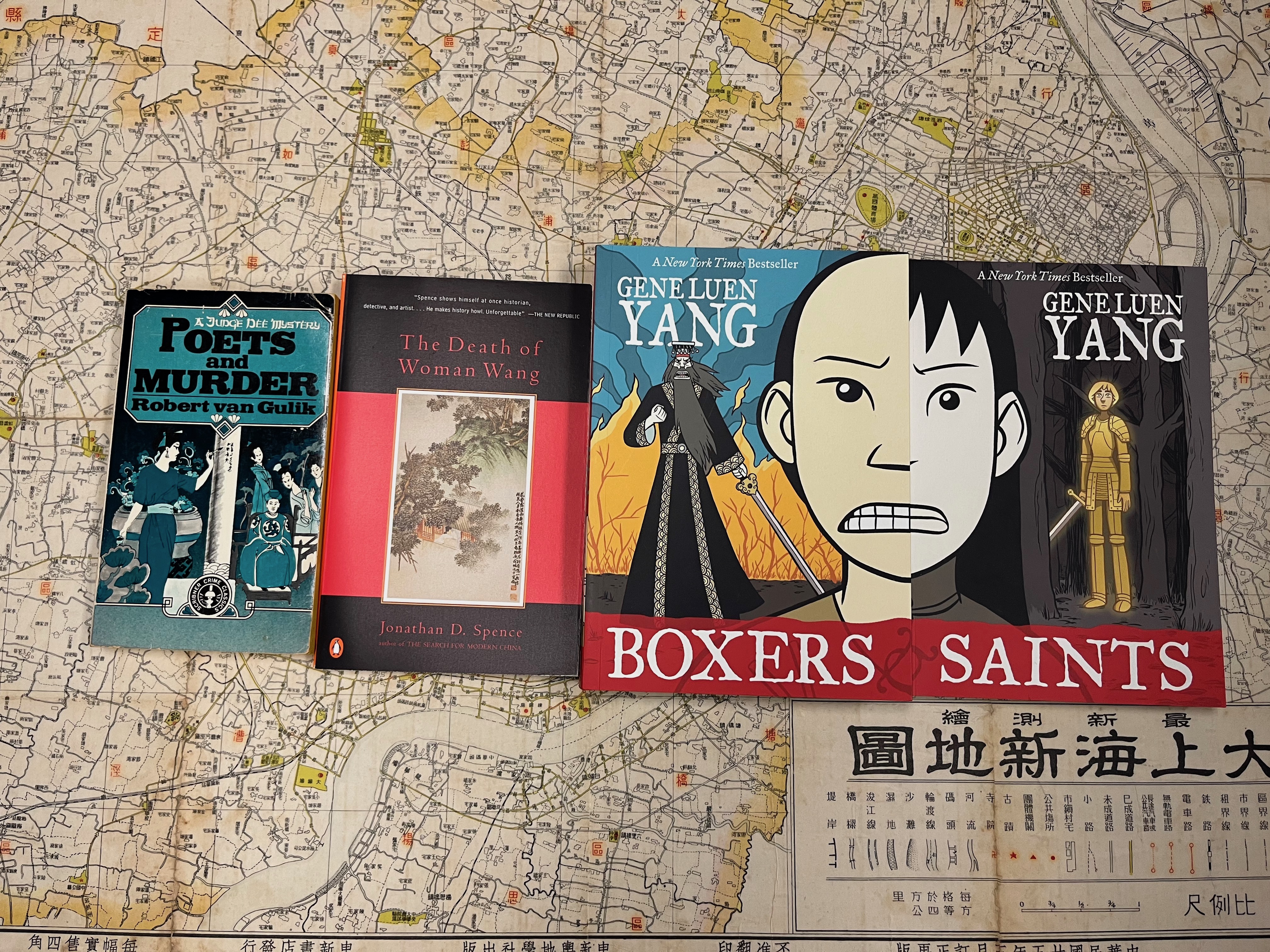 Four books lie on top of a historic map of Shanghai. The books are Poets and Murder, The Death of Woman Wang, Boxers, and Saints.