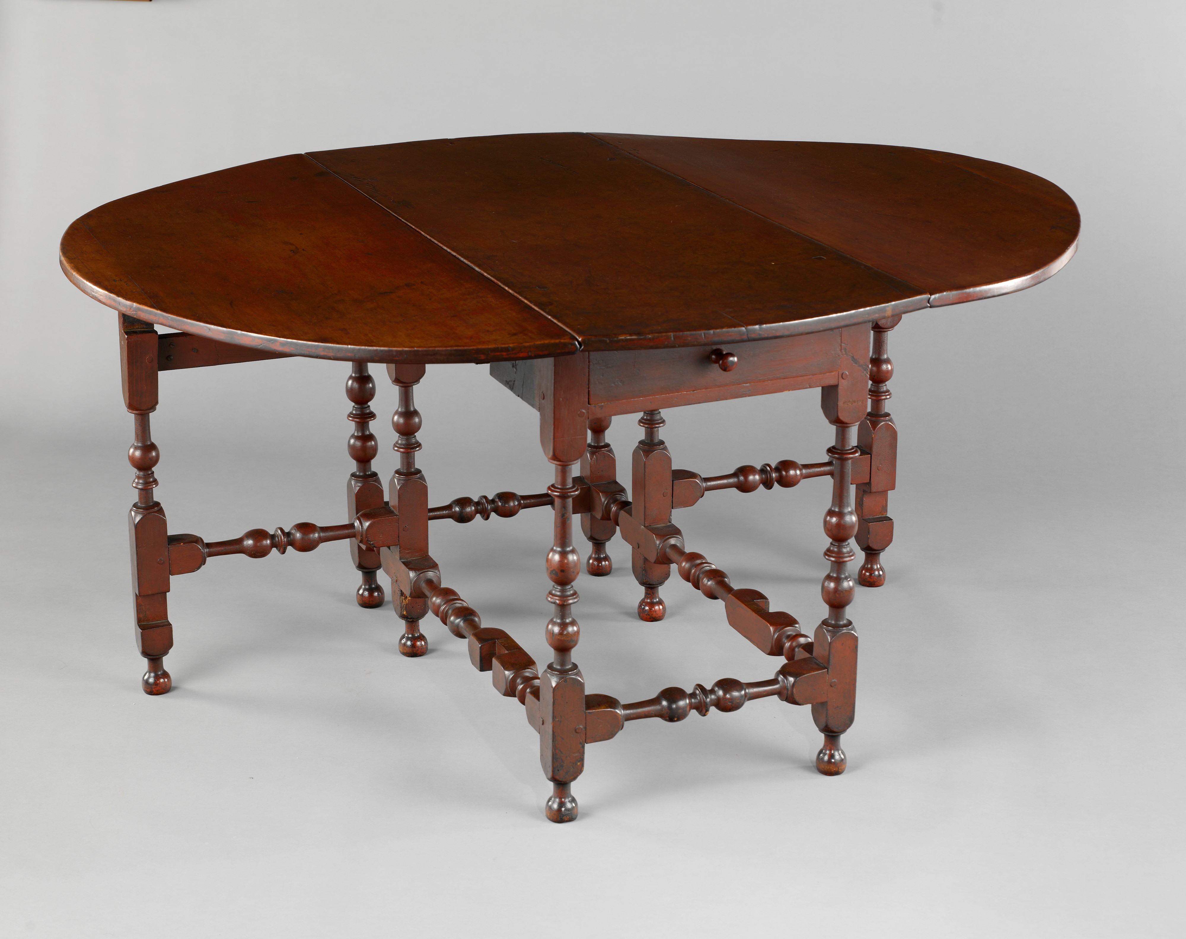 A reddish brown, oval table with two falling leaves. The legs of the table have a globe-shaped base, and a long, straight, tapering neck with a pronounced ring at the top. Two of the legs are open, like gates, to support the leaves.