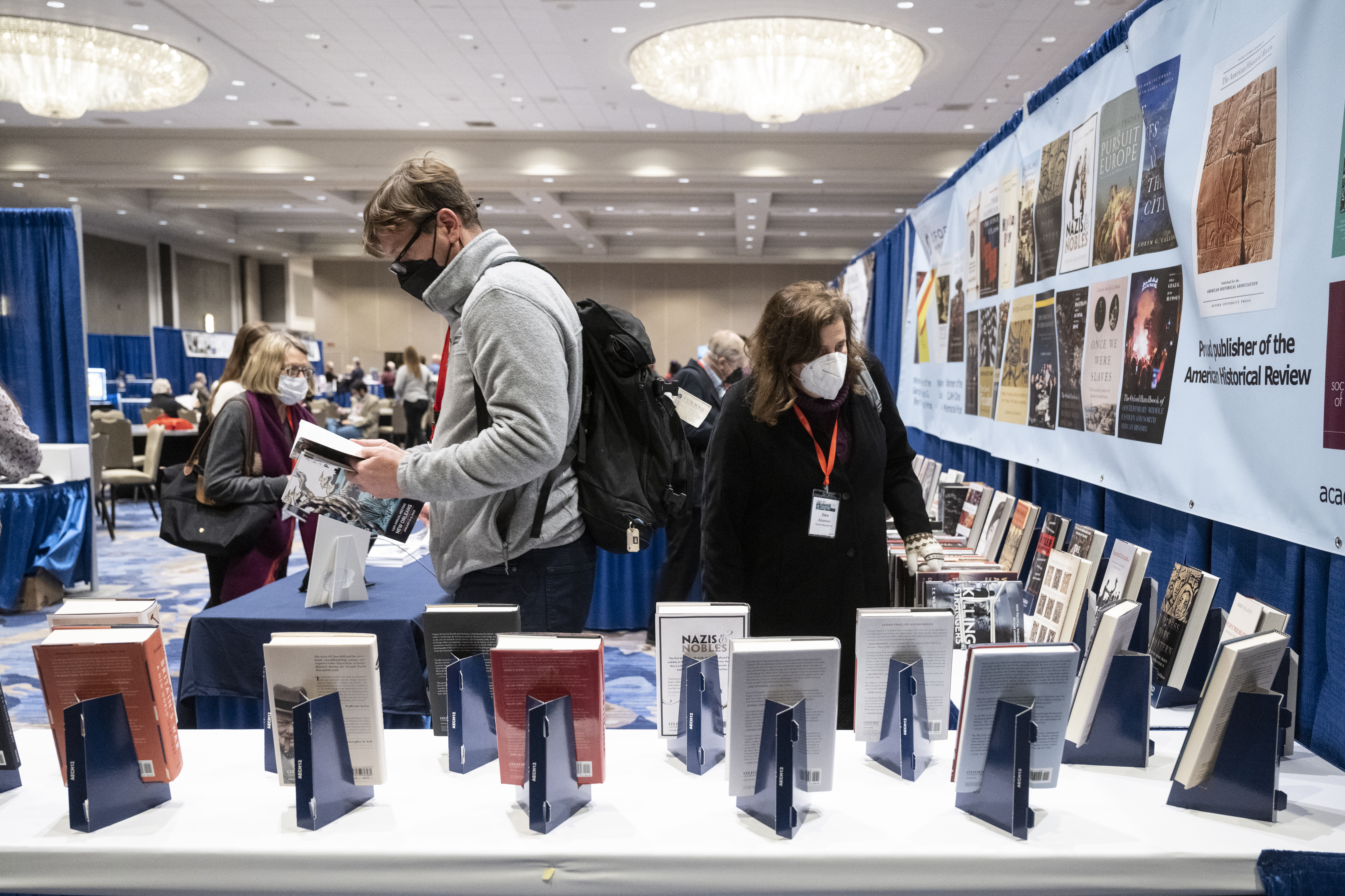 An exhibit hall booth at the AHA22 annual meeting, there are long tables with books on display and conference attendees looking at and reading the publications.