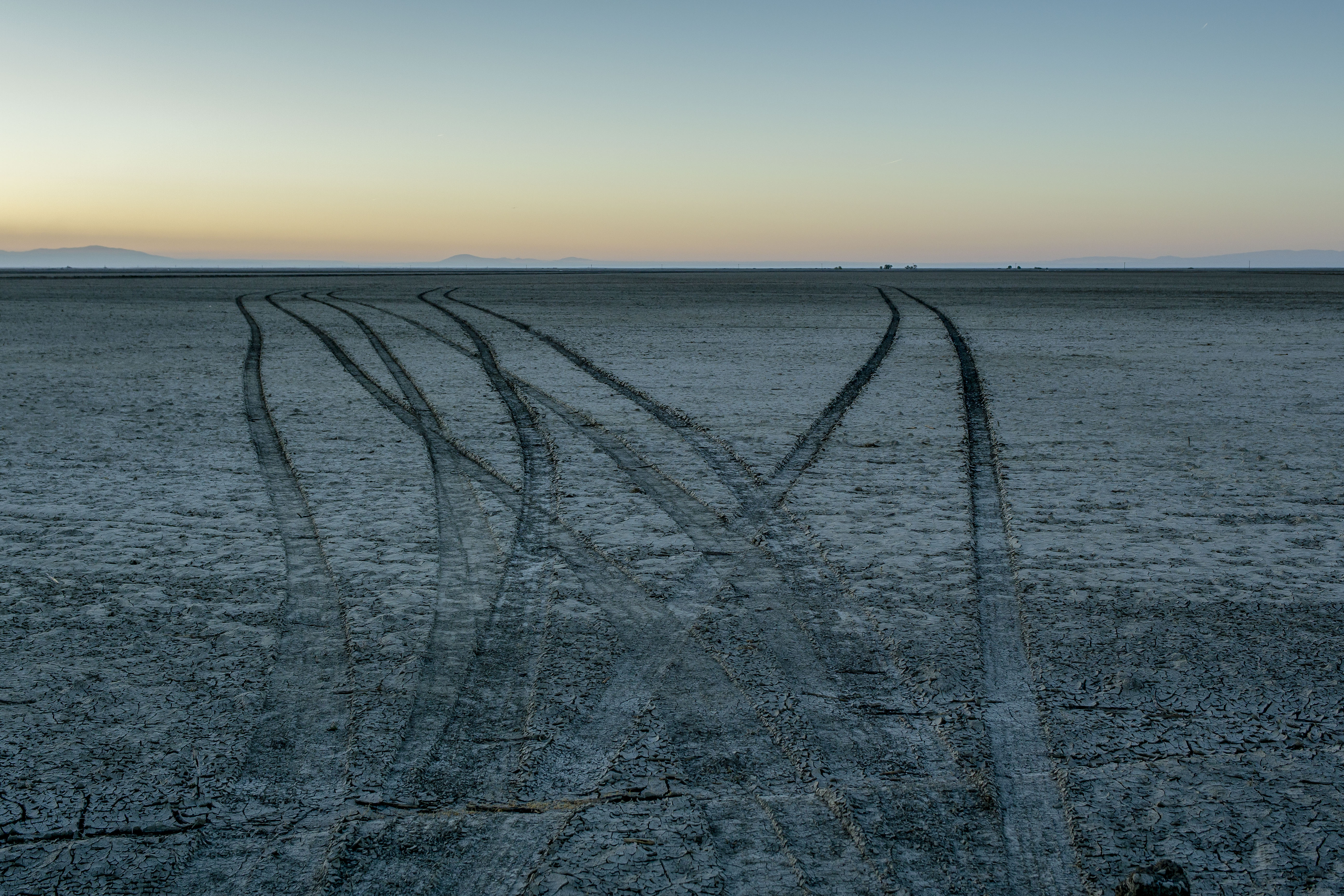 A photograph of an empty lake bed with tire tracks running through the sand.