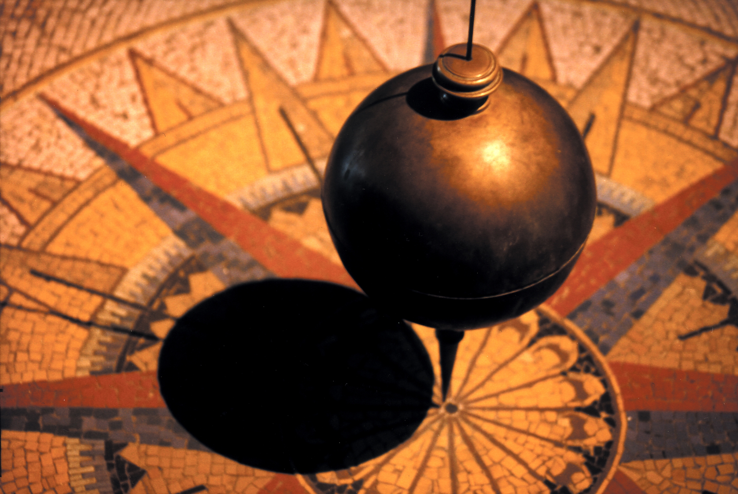 A brass pendulum hangs over a mosaic compass rose.