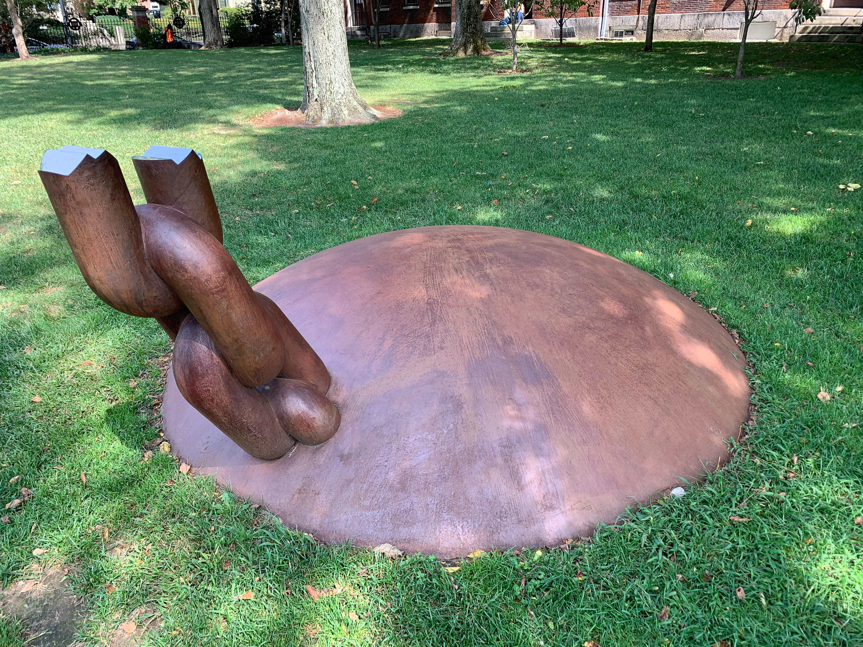 A bronze sphere in embedded in a campus green, with a chain coming out of part of it. The third link of the chain is broken and jagged, but polished to a mirror shine.