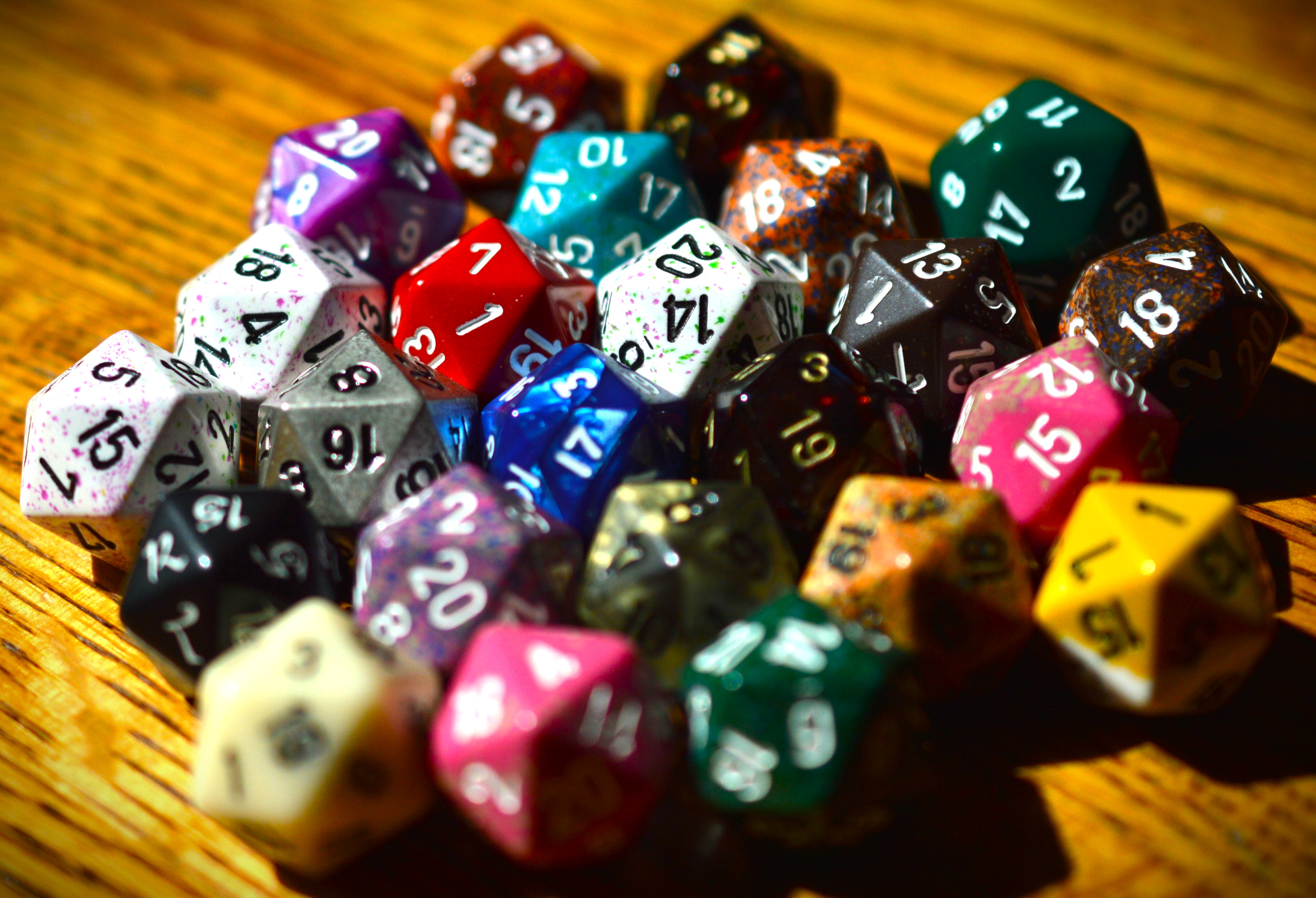 A pile of 20-sided dice in a variety of colors on a wooden table.