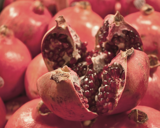 A quartered pomegranate rests on a bed of whole fruits.