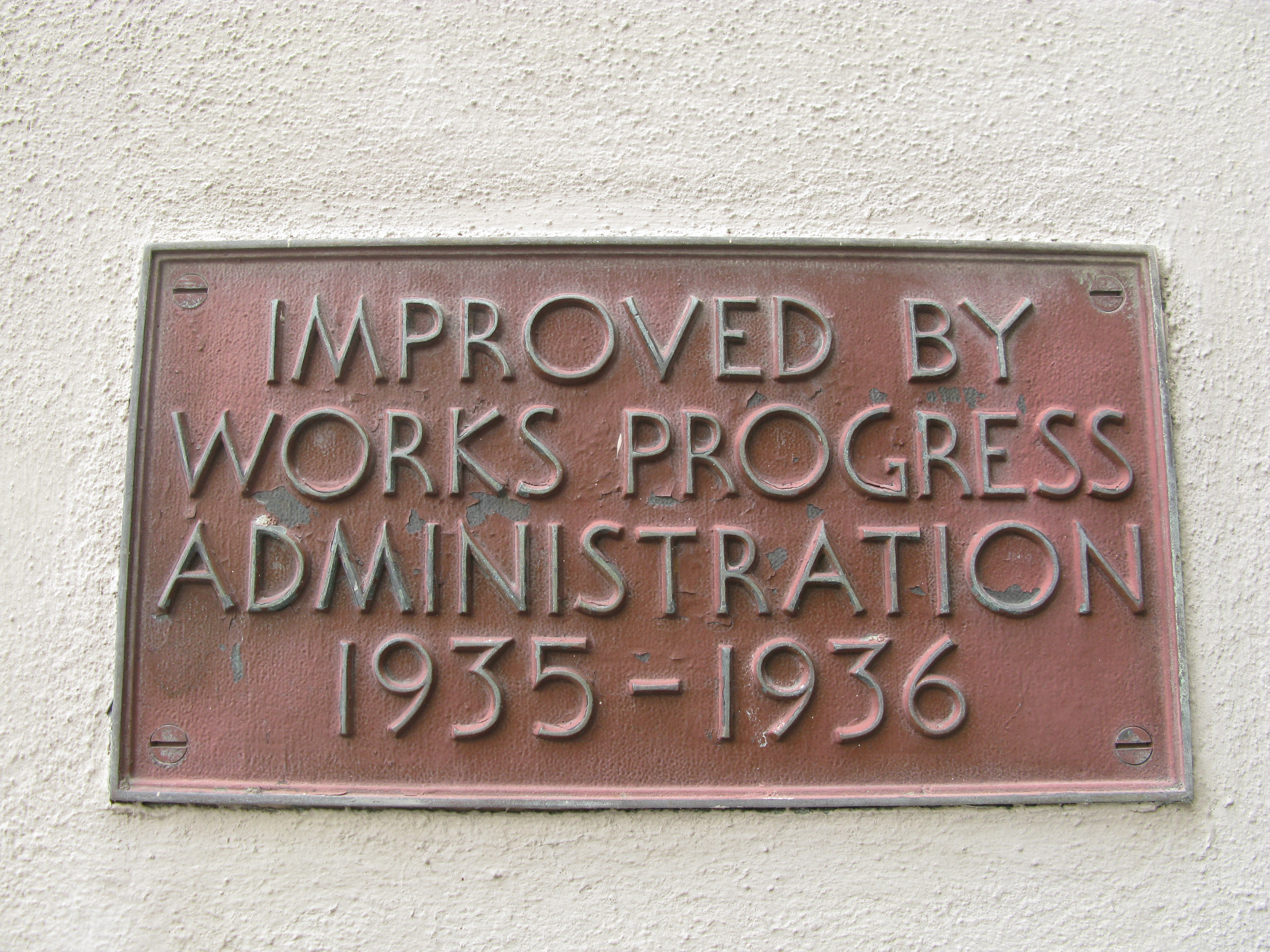 A brown plaque in a white wall with an art-deco font, reading 'Improved by Works Progress Administration 1935–1936'.