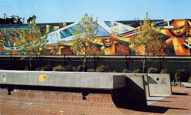 A mural of human figures holding up a train's beams and its trains on their backs above a train rail