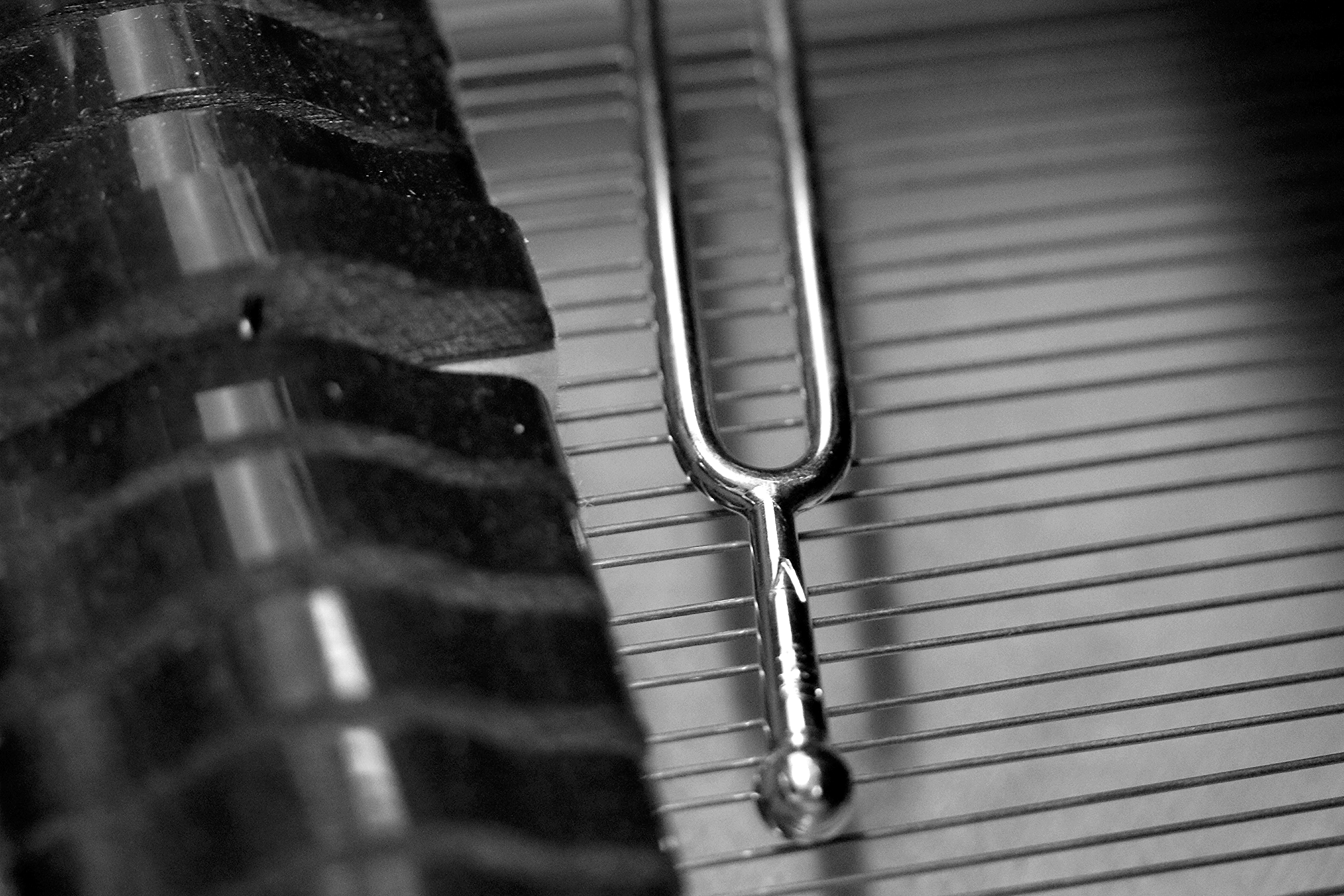 A silver tuning fork rests on the interior wires of a piano.