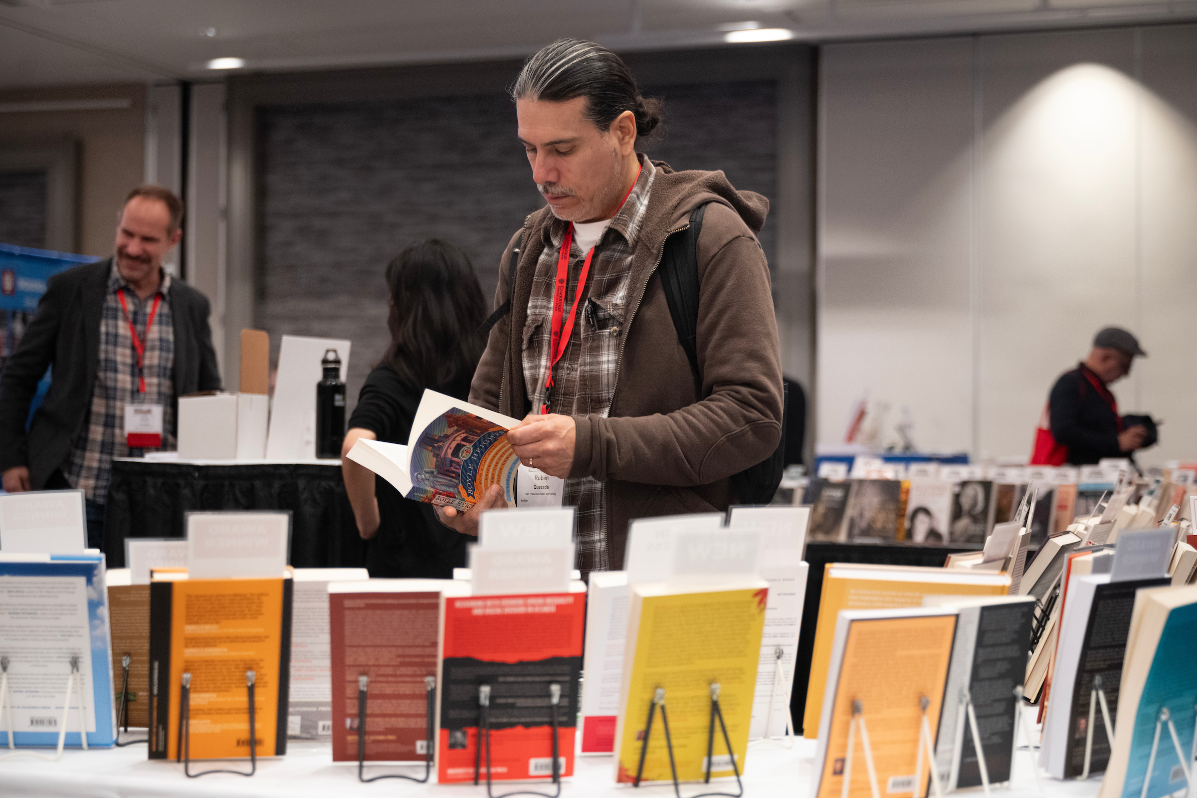 A man holding a book open in front of a booth with lots of books on display
