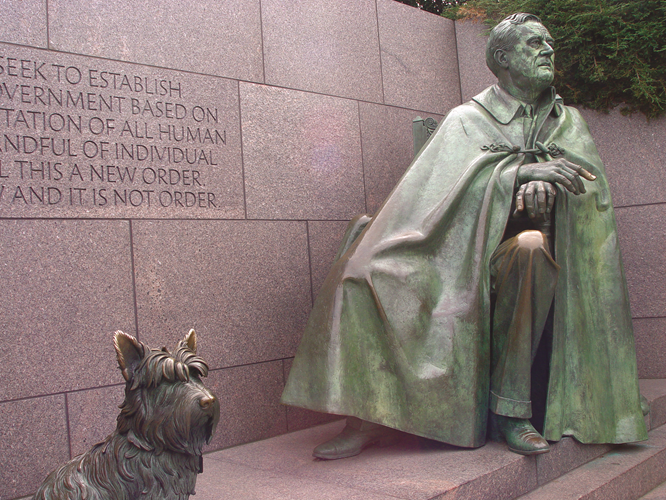 A statue of Franklin Delano Roosevelt seated, wearing a clak that covers his body, with his dog Nala seated at his feet