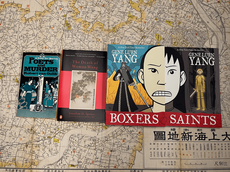 Four books lie on top of a historic map of Shanghai. The books are Poets and Murder, The Death of Woman Wang, Boxers, and Saints.