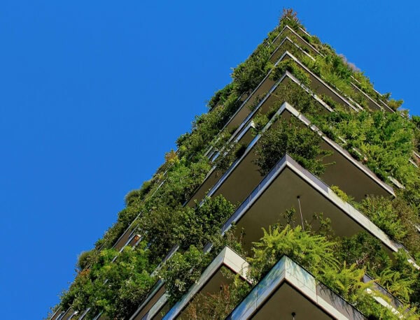 Green vegetation hangs off every level of a skyscraper, set against a clear blue sky.