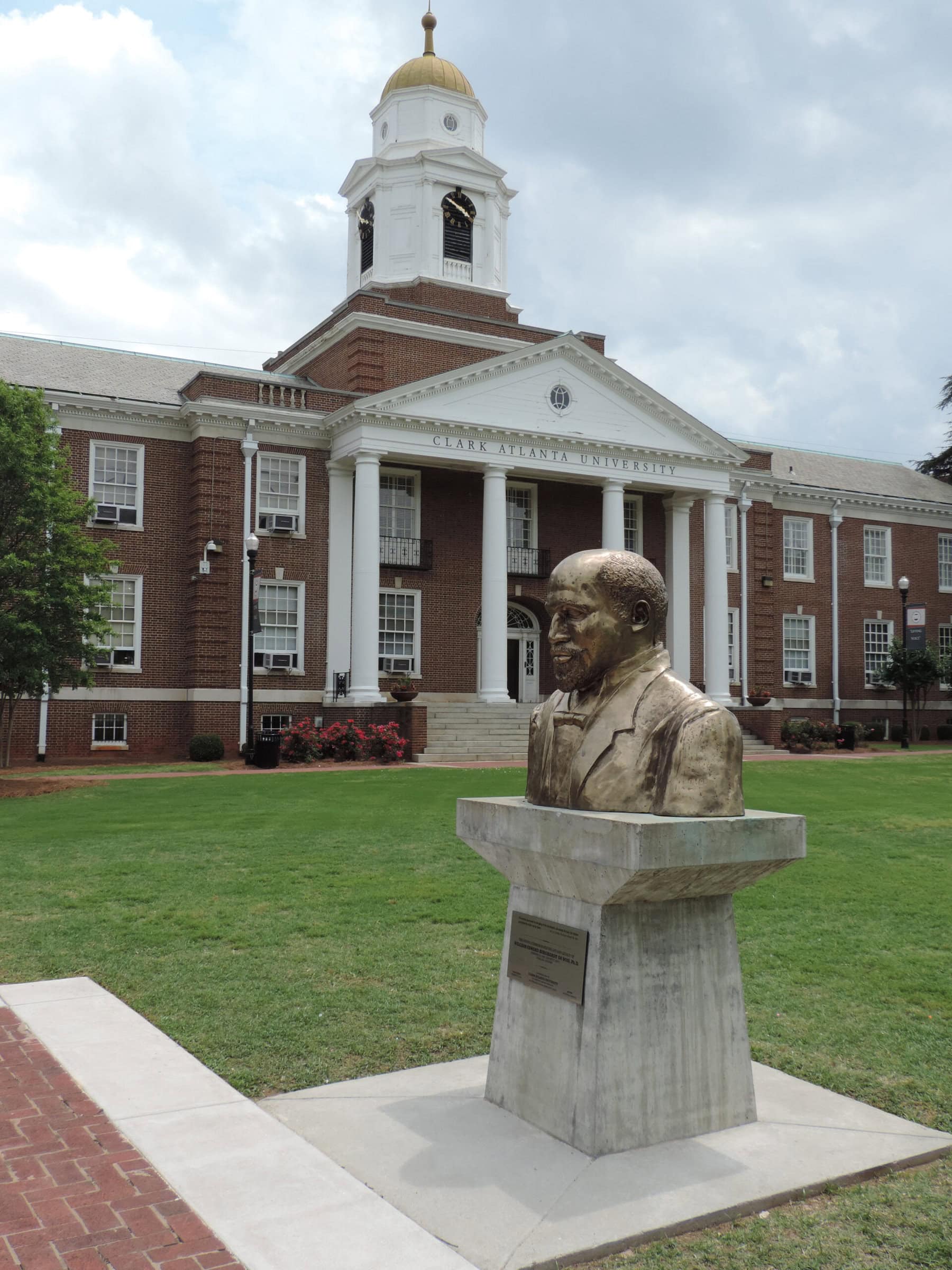 A white and brick building overlooking a statue