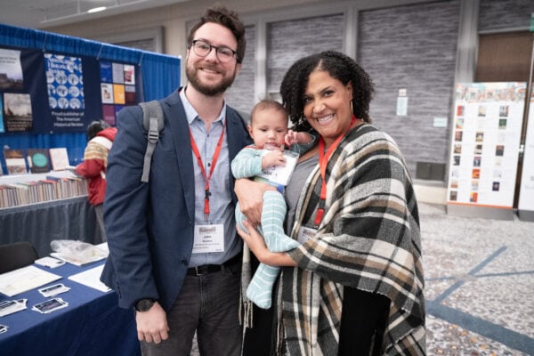 A white man wearing a suit smiling next to a Black woman holding a baby smiling