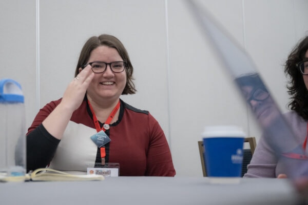 A white woman with short brown hair and glasses smiling on a panel