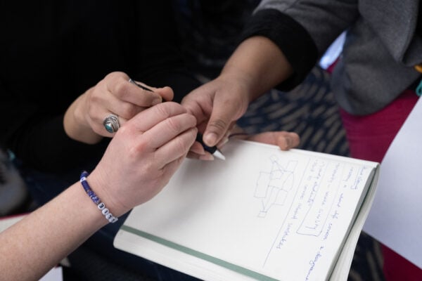 Three hands holding the same pen over a notebook