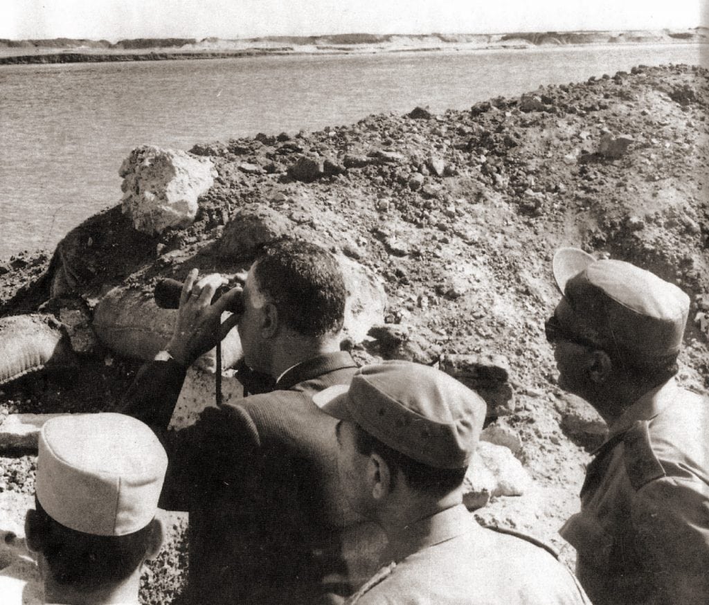 Black and white photo of President Nasser standing greeting a group of people.