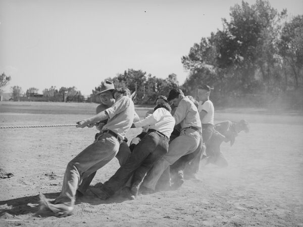 Black and white image of a group of men pulling a rope towards them in a game of tug-of-war