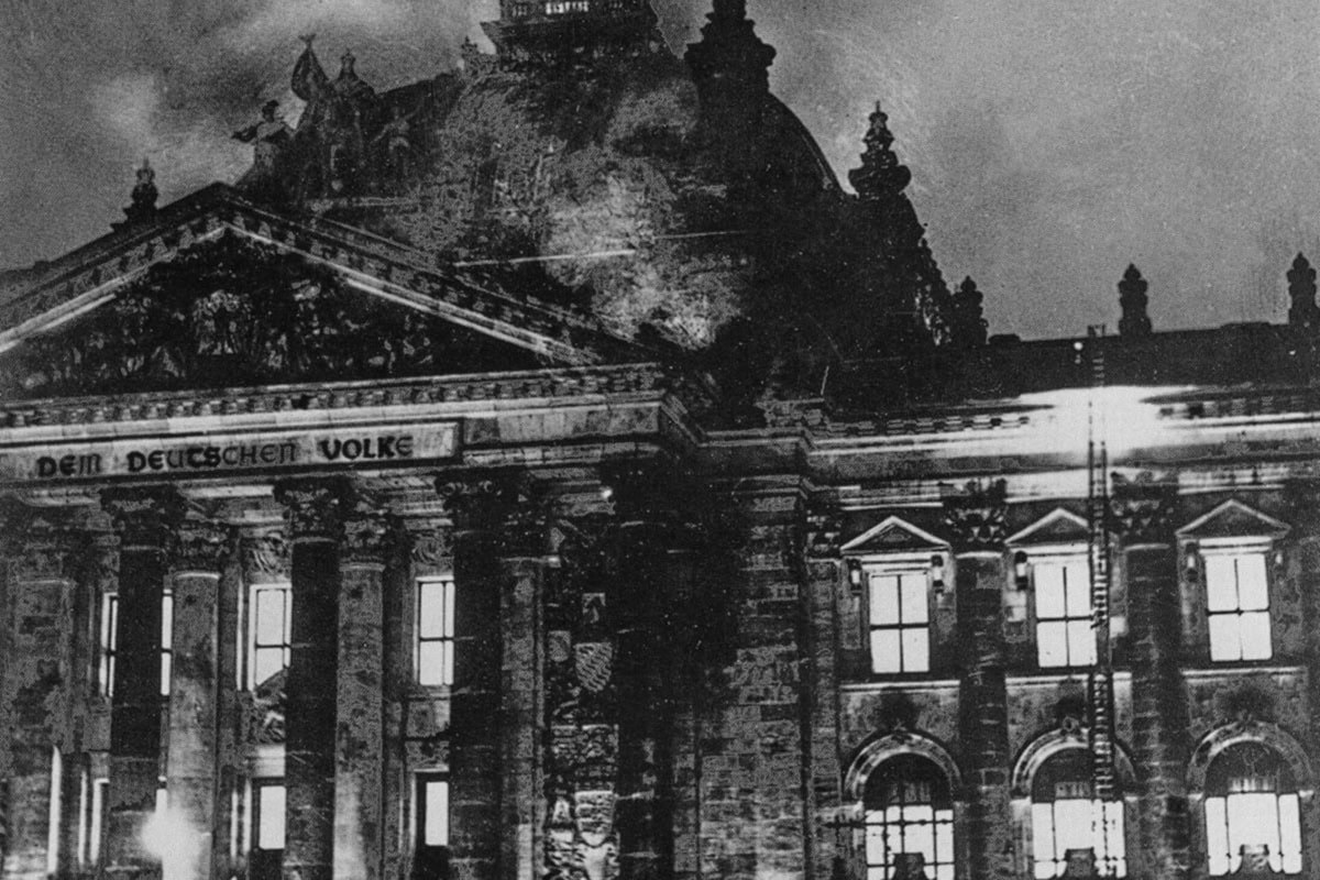 Black and white photograph showing firefighters struggling to put out the fire in the Reichstag building. Billows of smoke can be seen above the ornate building.