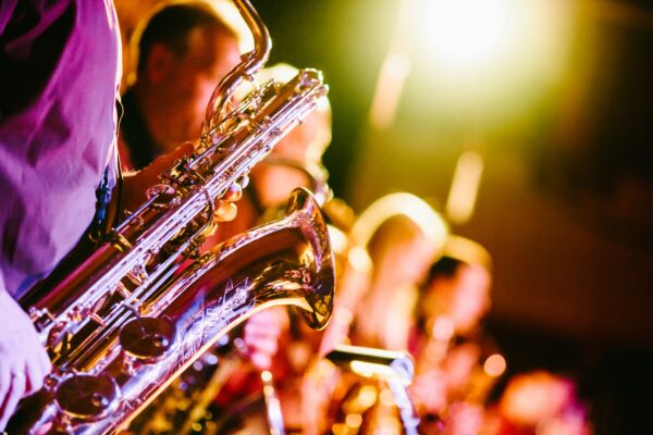 A close-up of a saxophone being played with the rest of a band blurred behind it