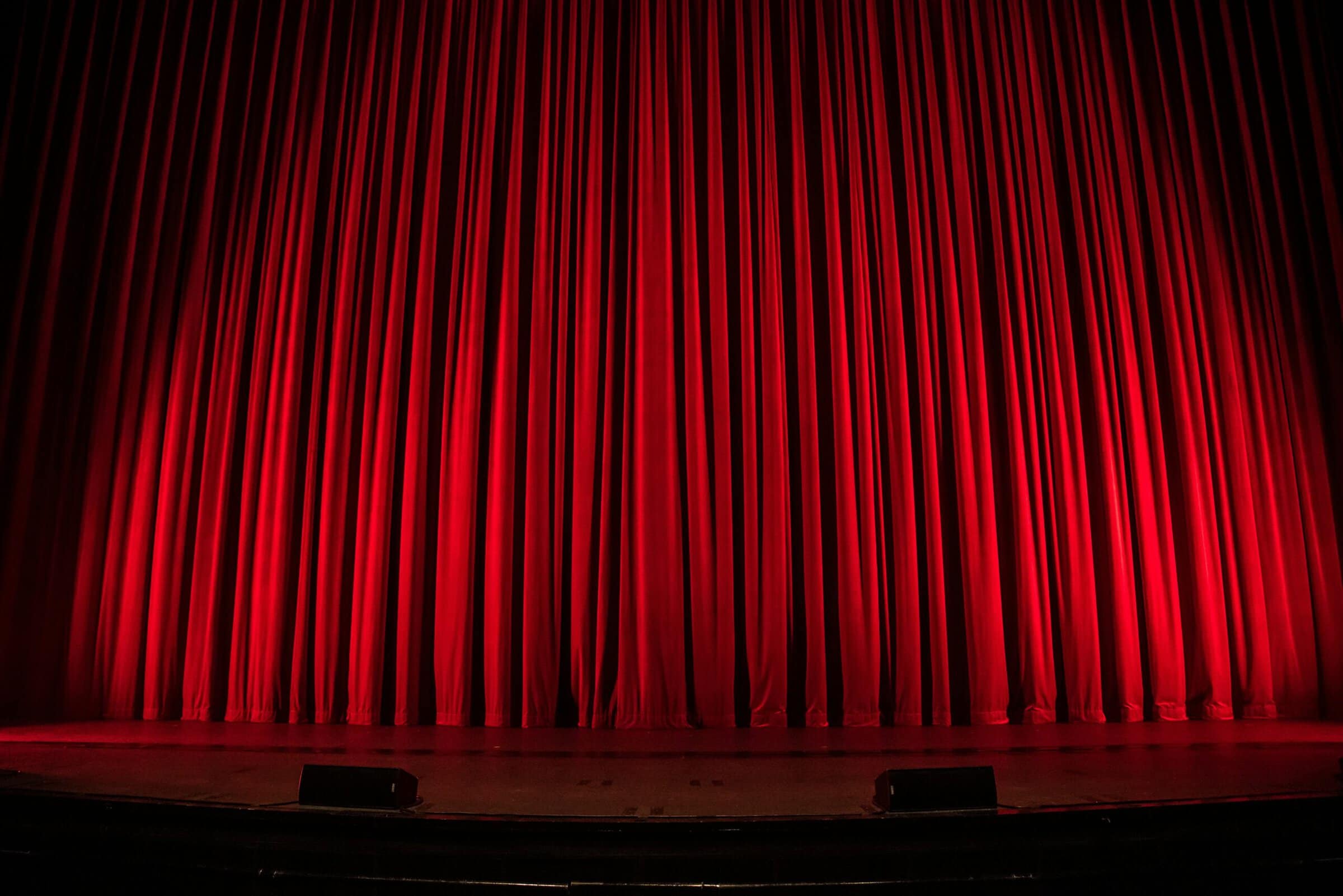 A red curtain hangs above a stage, with bright light cast upon the center.