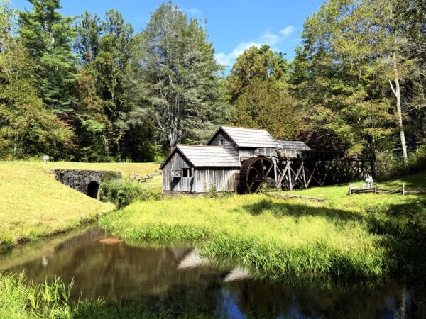 A small building and mill surrounded by grass and large trees