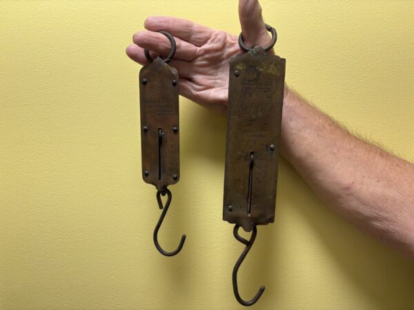 A hand holding up two brass scales against a yellow background