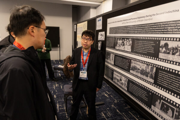A man standing in front of a poster with his hand out explaining it to another man