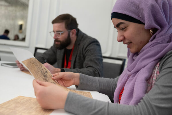 A woman wearing a purple hijab holding and examining a map in front of her face