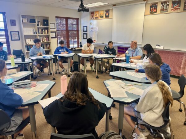 A group of high schools students sitting at desks in a circle