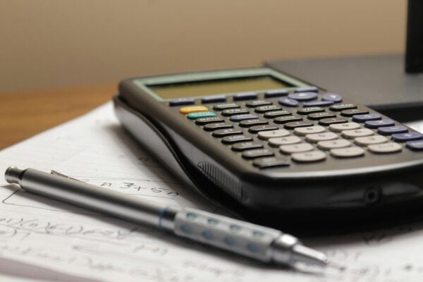 A calculator and a pen rest on sheets of mathematical equations.