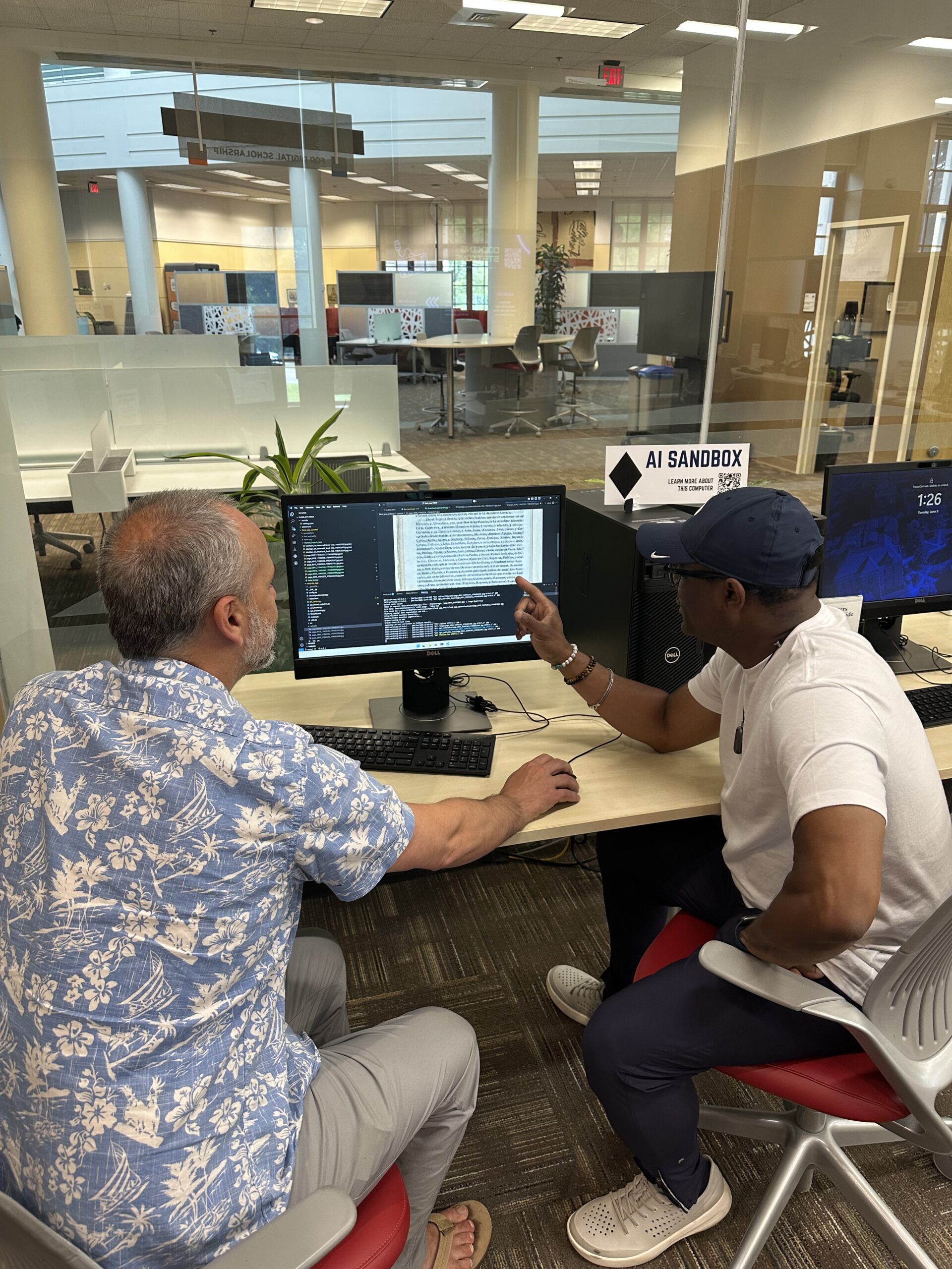 Two men sit at a computer in a library